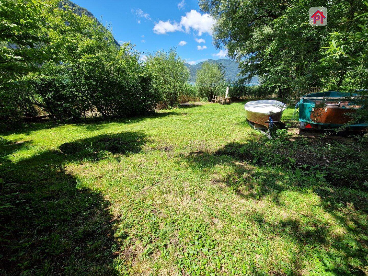 Gepflegte Rasenfläche im Garten mit Blick auf den See und abgestellten Booten.