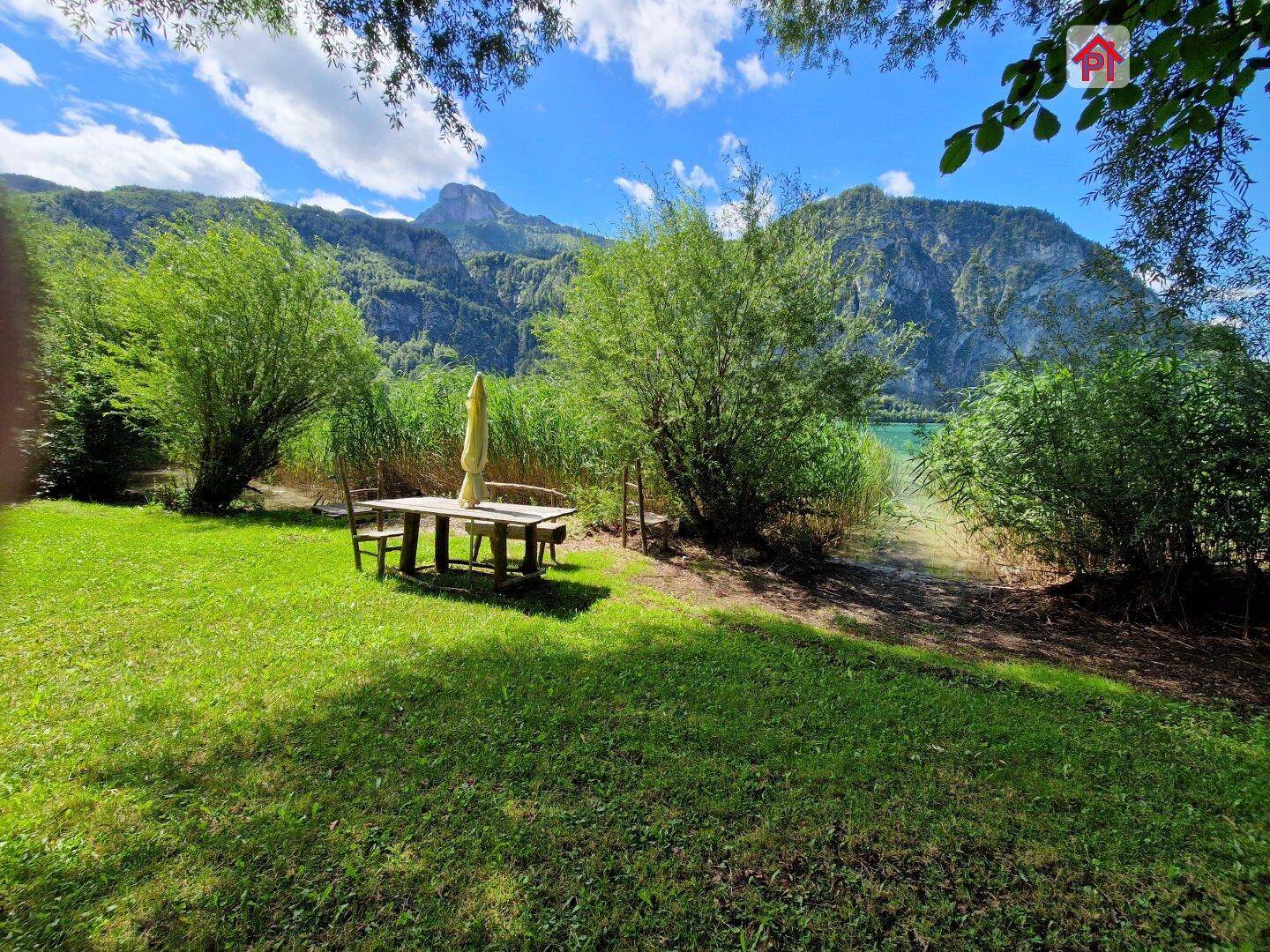 Sonniger Gartenbereich mit Esstisch und Sonnenschirm direkt am See mit Bergblick.