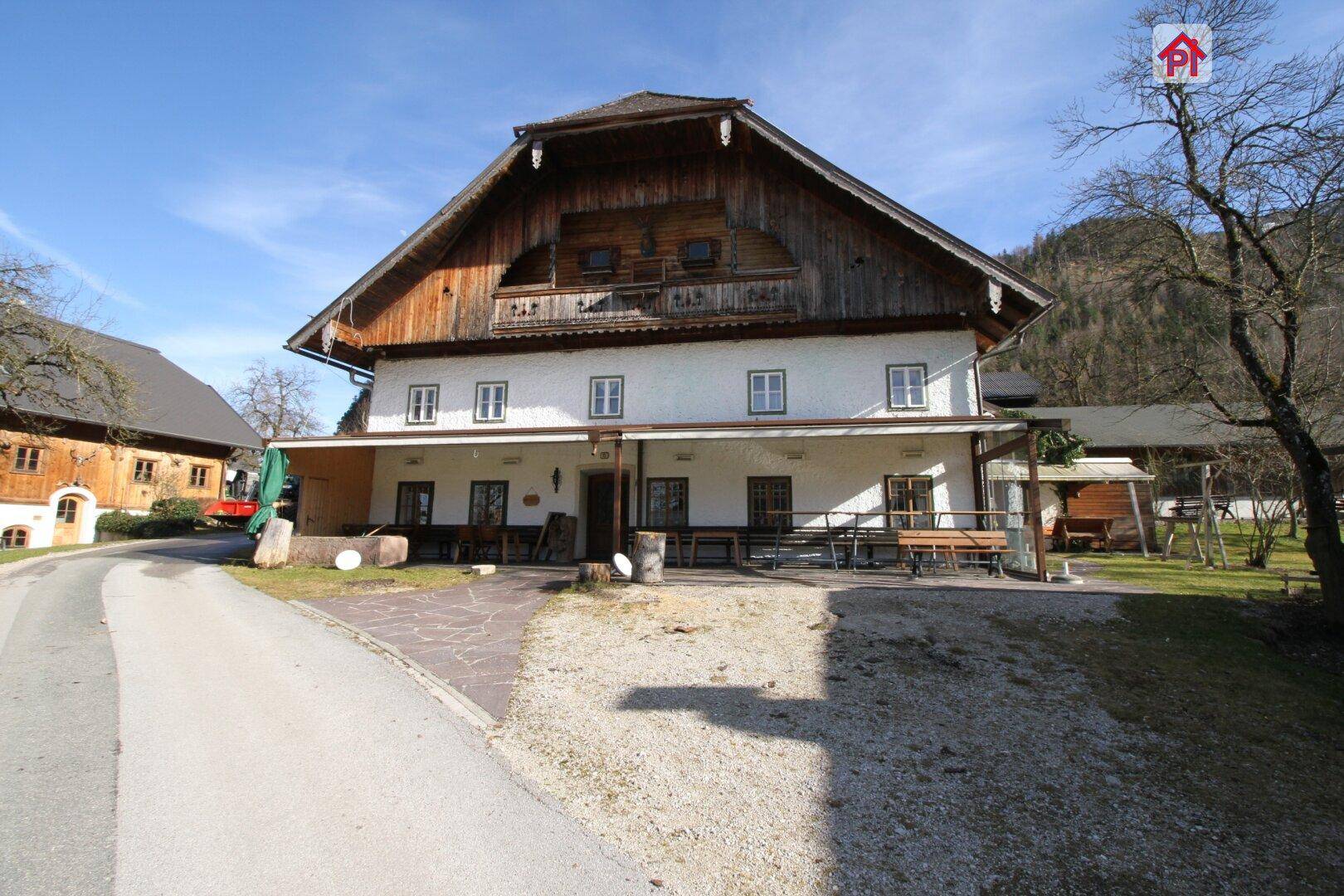 Vorderansicht eines traditionellen Gebäudes mit Holzbalkonen und einer Mischung aus Holz- und Putzfassade, umgeben von Natur.