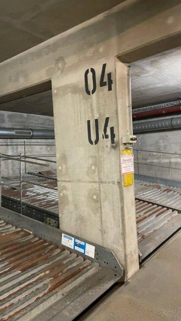 Tiefgarage mit Duplex-Parksystem, nummeriertem Betonpfeiler und sichtbaren Installationen.