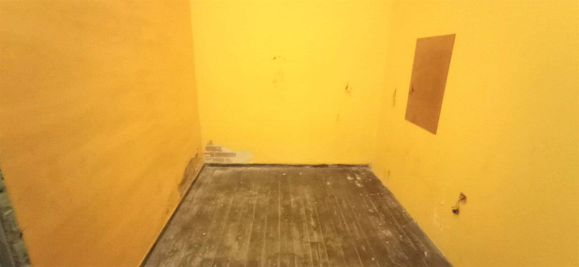 Leerer Raum mit gelben Wänden und abgenutztem Holzboden, der eine Renovierung benötigt.