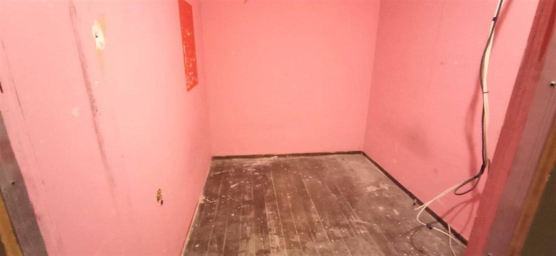 Kleiner, leerer Raum mit rosa Wänden und abgenutztem Holzboden, bereit für Renovierung.