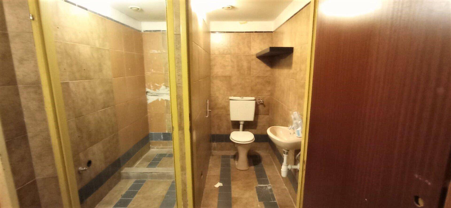 Badezimmer mit braunen Fliesen, Toilette und Waschbecken, das eine Modernisierung benötigt.