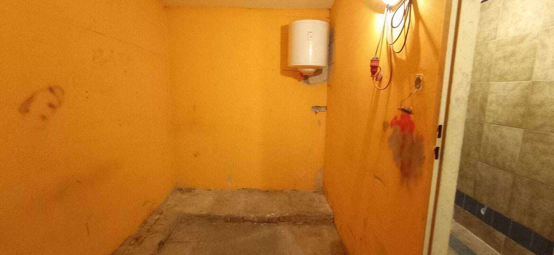 Lagerraum mit orangefarbenen Wänden, Betonboden und einem Warmwasserbereiter an der Wand.