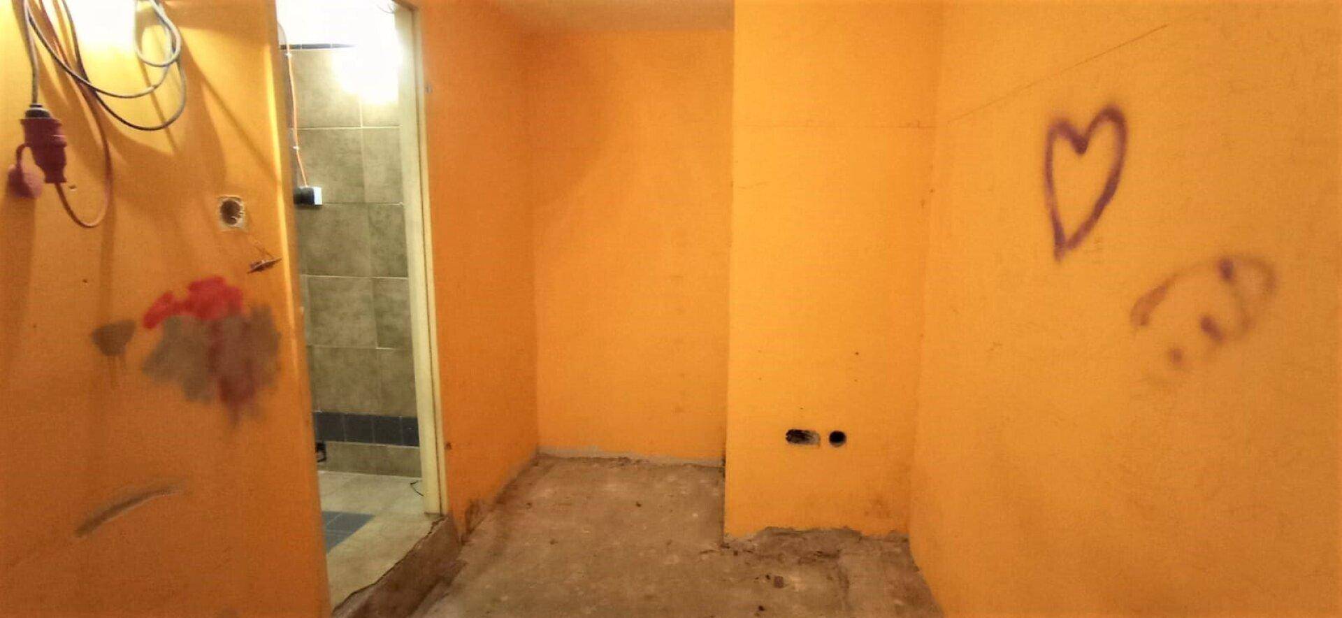 Leerer Raum mit orangefarbenen Wänden, Betonboden und Graffiti, der eine umfassende Renovierung erfordert.