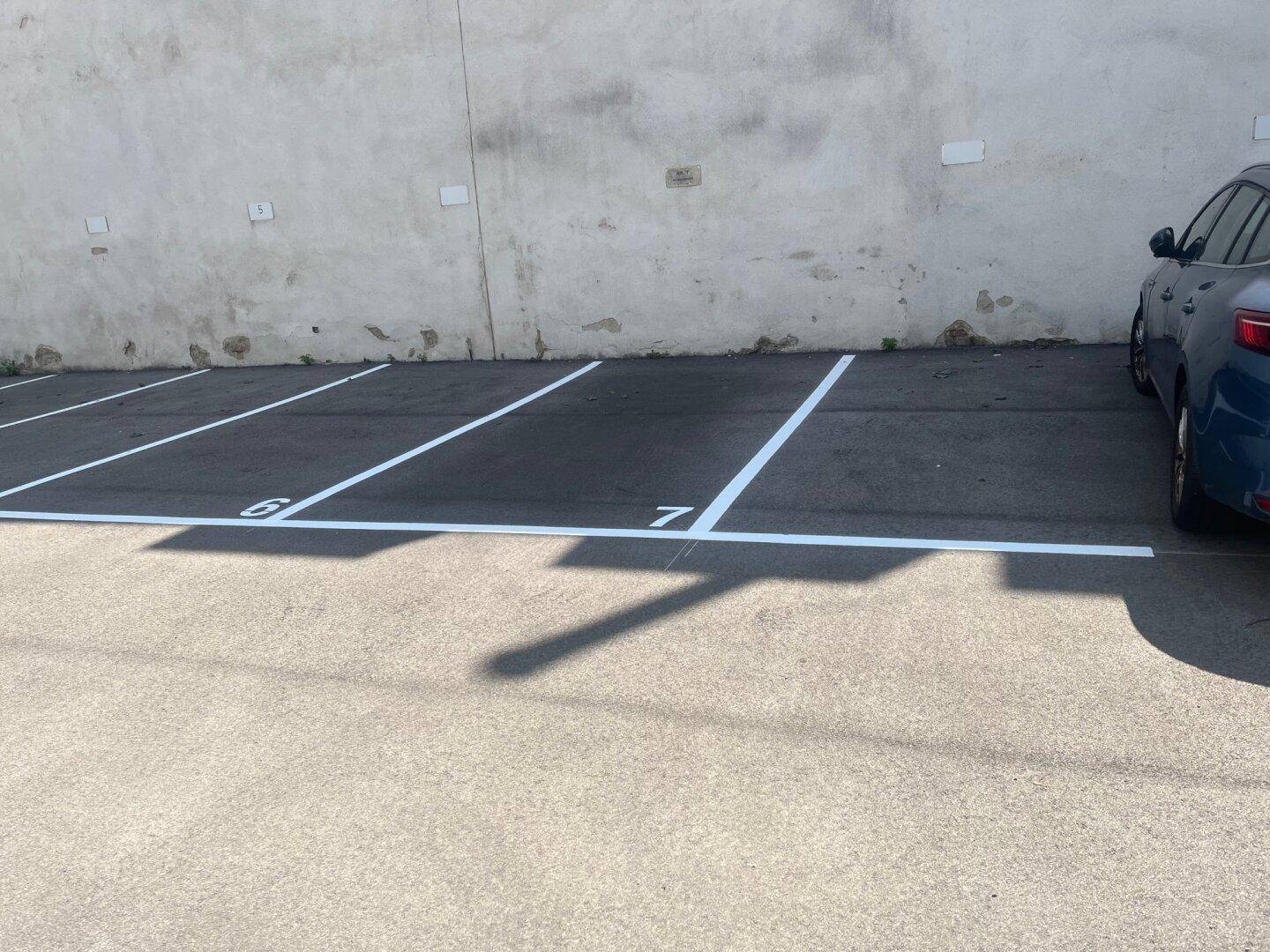 Weitere markierte Außenparkplätze auf Asphalt mit weißen Linien und Schattenwurf.