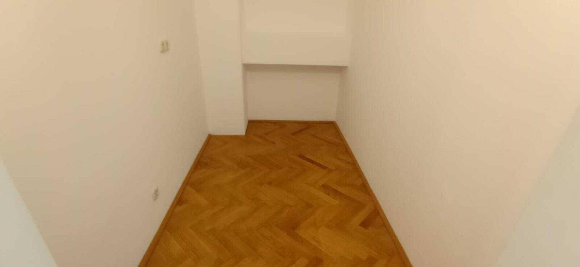 Schmaler Raum mit Fischgrätparkettboden und weißen Wänden, ideal als Abstellraum oder begehbarer Kleiderschrank.