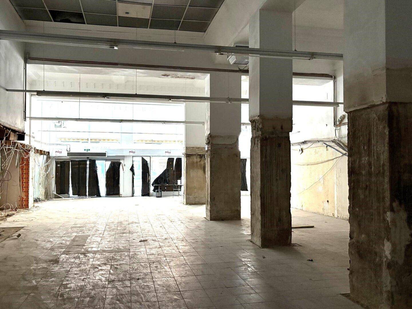 Weitläufiger Gewerberaum mit Säulen und großen Fenstern zur Straße, derzeit im Zustand der Entkernung.