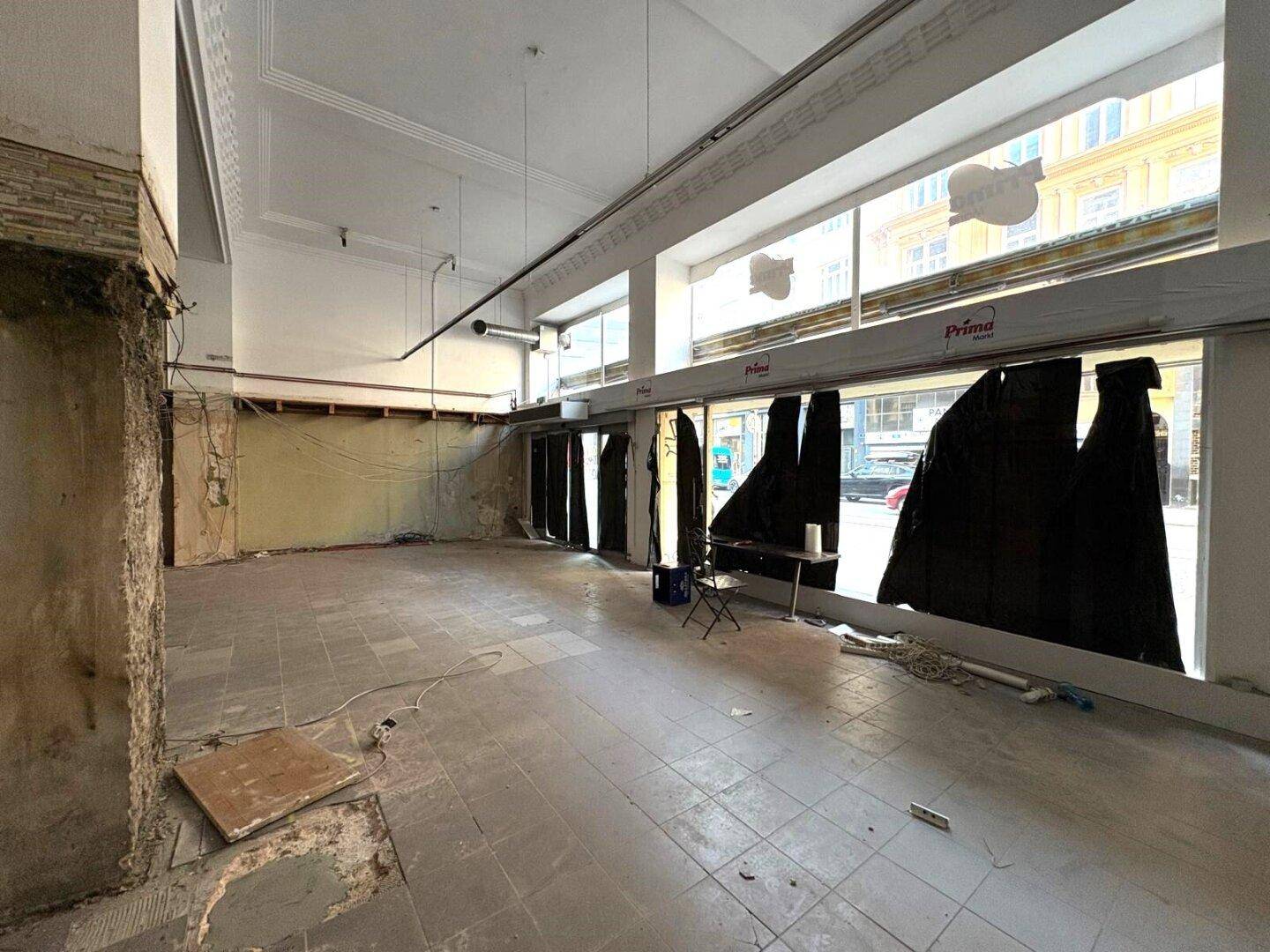 Großer, offener Gewerberaum mit breiter Fensterfront zur Straße, im Rohbauzustand mit sichtbaren Wänden.