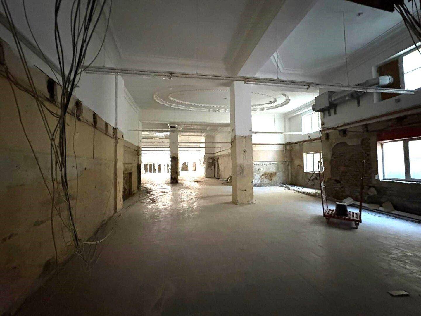Geräumiger Gewerberaum mit hohen Decken und Säulen, im Rohbauzustand mit sichtbaren Installationen und Fenstern.