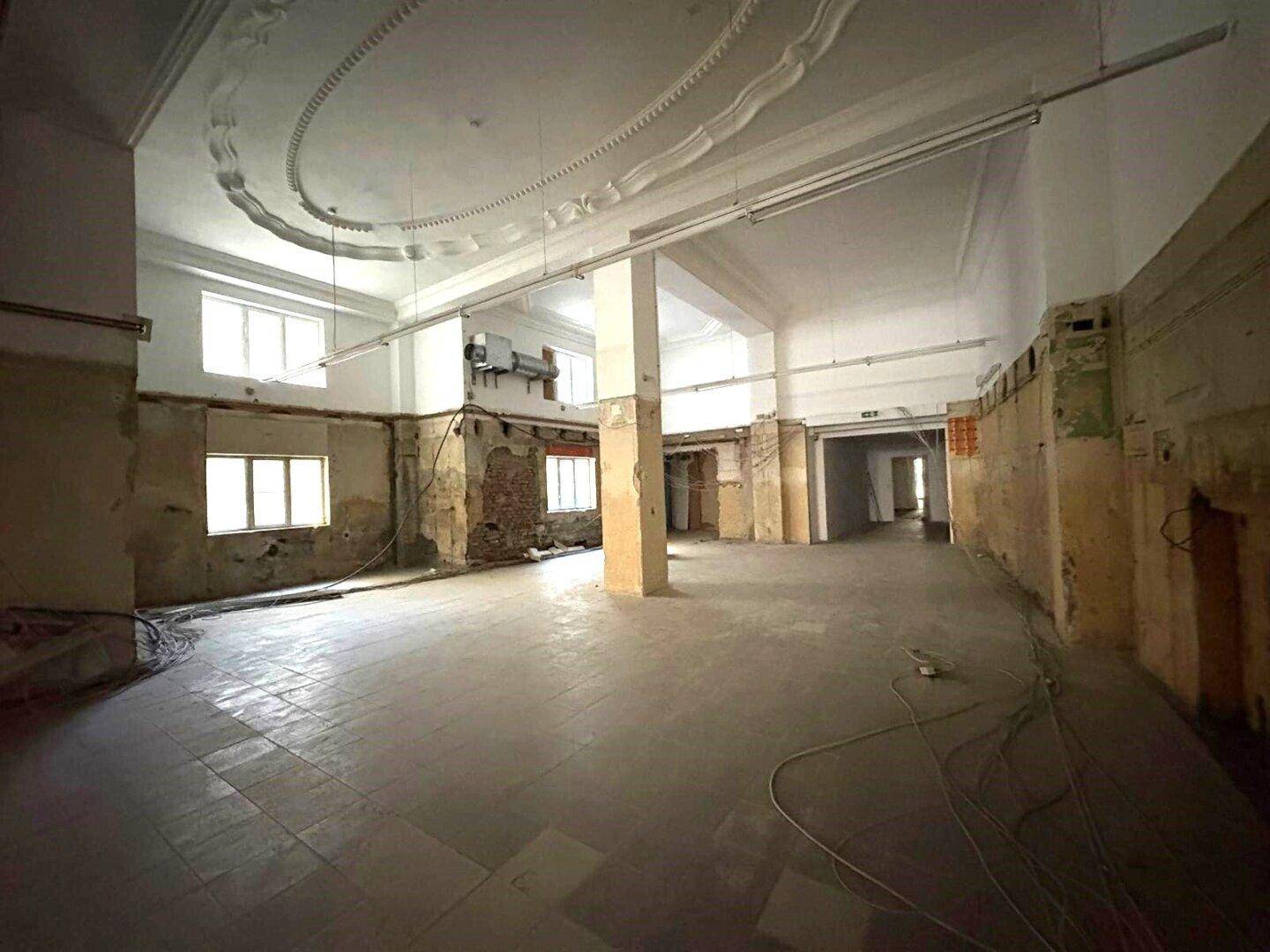 Großer, offener Gewerberaum im Rohbau mit hohen Decken und dekorativen Stuckelementen, bereit für den Ausbau.