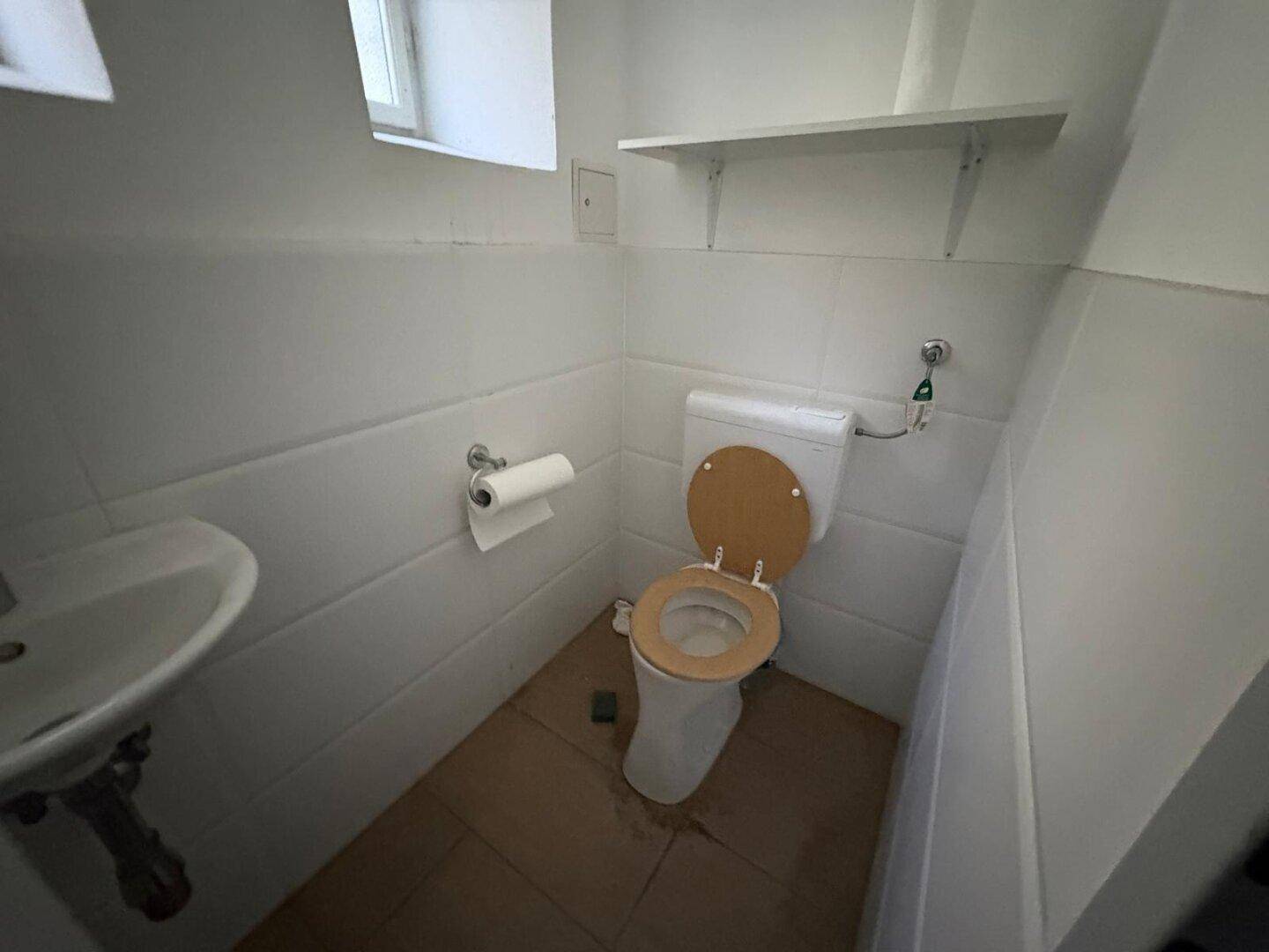 Kleines Badezimmer mit Toilette, Waschbecken und einem kleinen Fenster, einfach und funktional gestaltet.