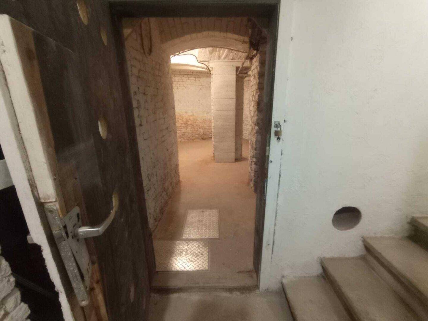 Blick durch eine offene Tür in den Kellerbereich mit Treppenabgang und Ziegelwänden.