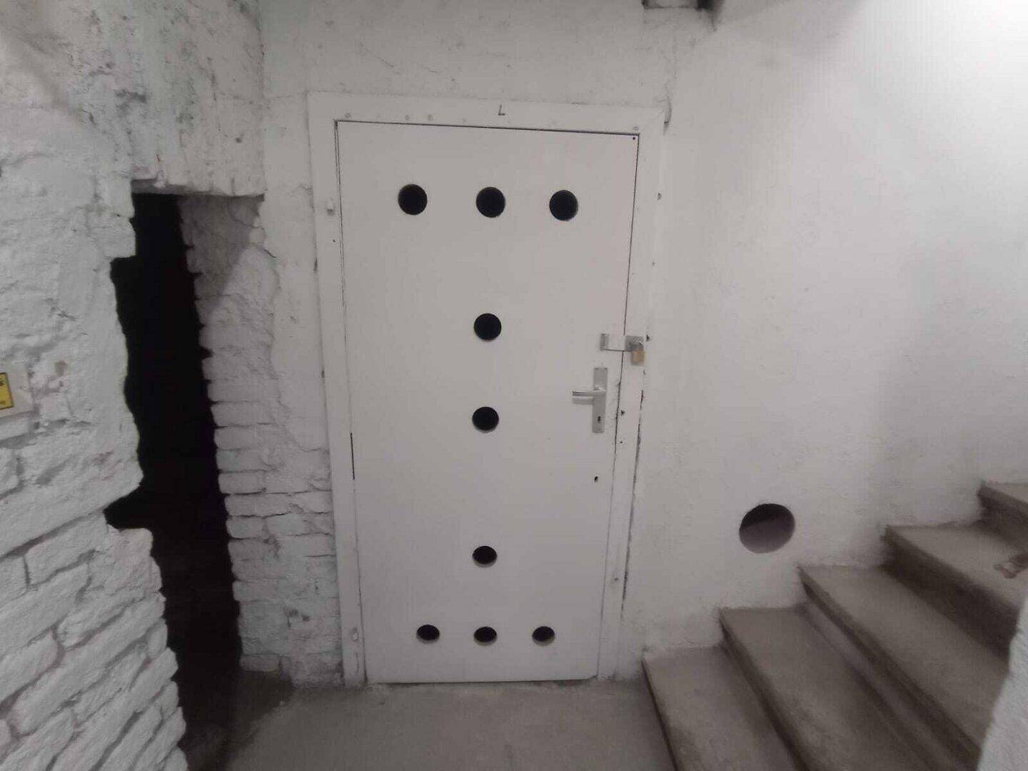 Weiße Kellertür mit runden Öffnungen neben einem Treppenabgang in den Keller.