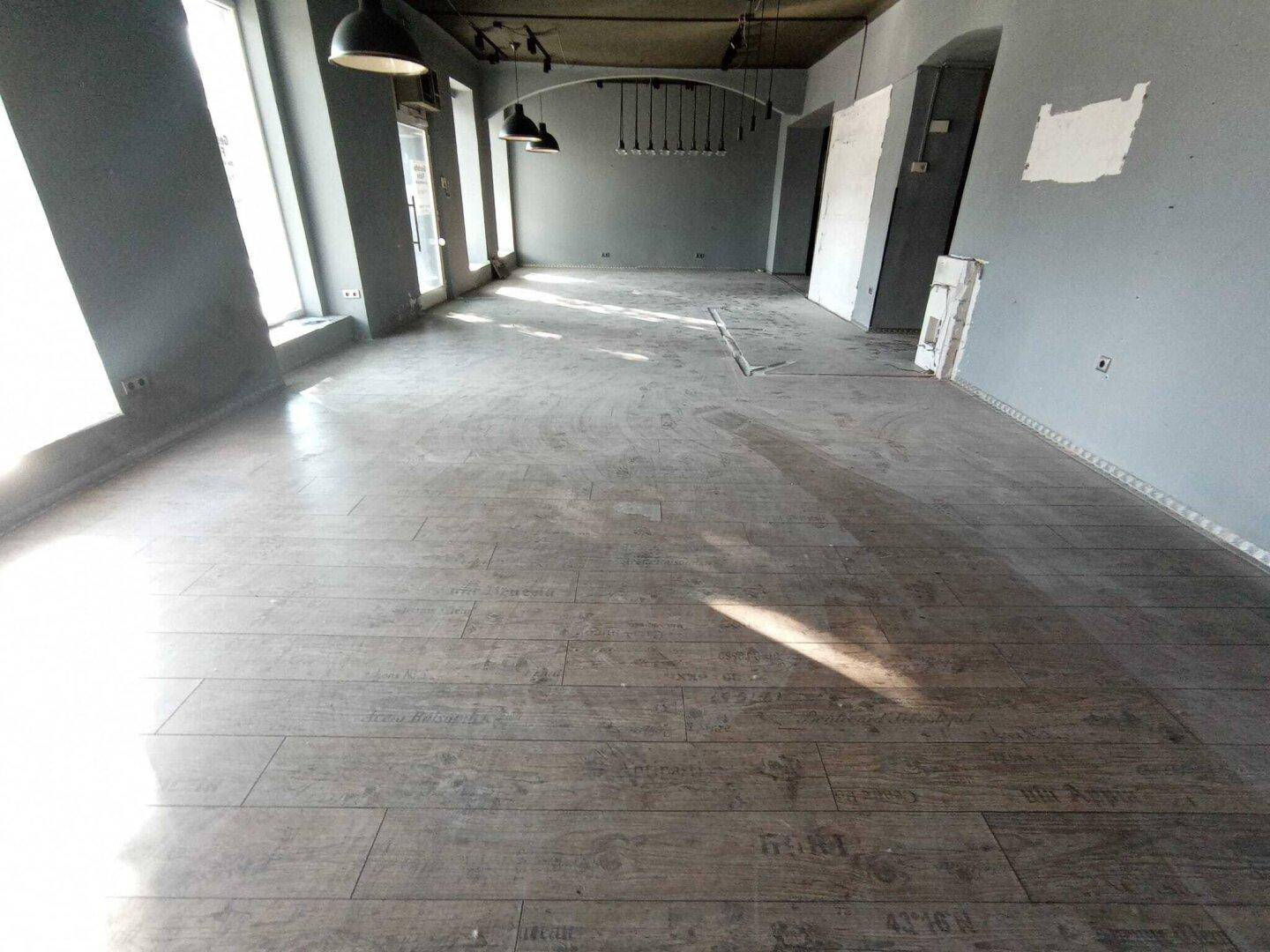 Geräumiger Innenraum eines Geschäfts mit Holzboden und großen Fenstern, die viel Tageslicht hereinlassen.