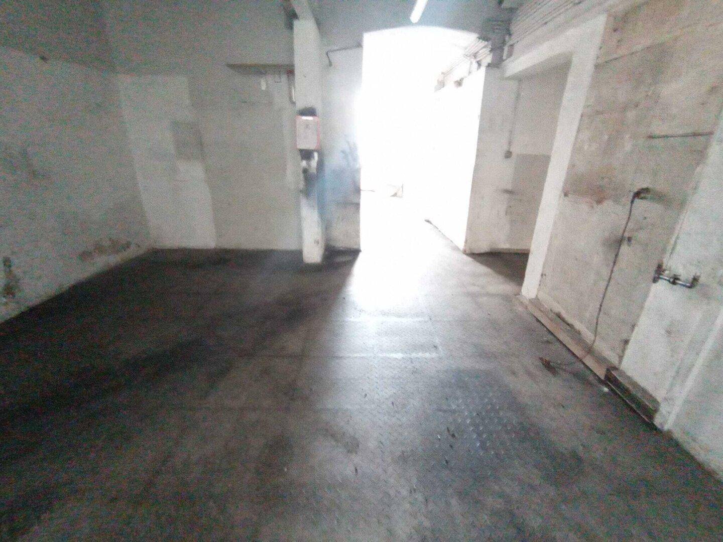 Langer, heller Lagerraum mit Betonboden und weißen Wänden, der zu weiteren Bereichen führt.