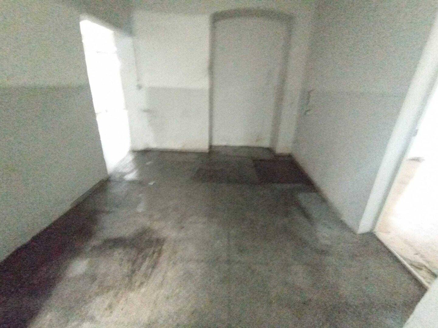 Einfacher Raum mit Betonboden und weißen Wänden, der als Lager oder Abstellraum genutzt werden könnte.