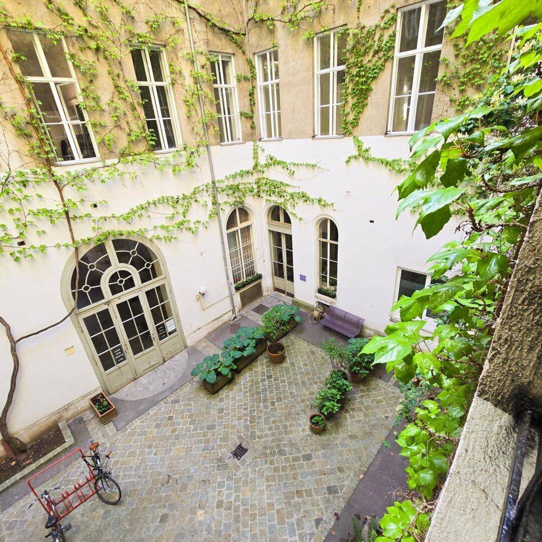 Blick von oben auf den begrünten Innenhof mit Kopfsteinpflaster und historischen Fenstern an den Fassaden.