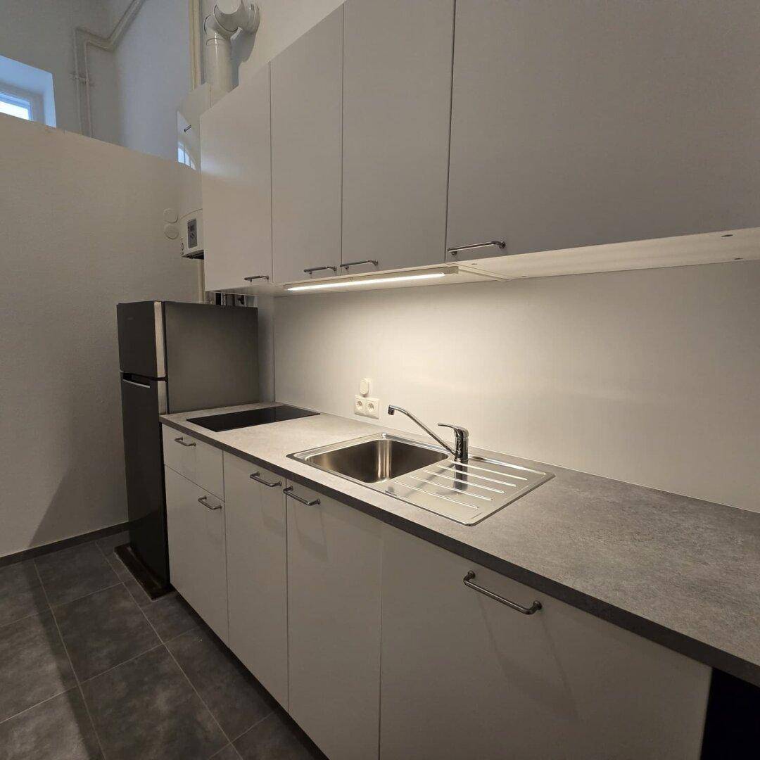 Helle Küchenzeile mit Spülbecken, Induktionskochfeld und modernen weißen Schränken, gut beleuchtet.