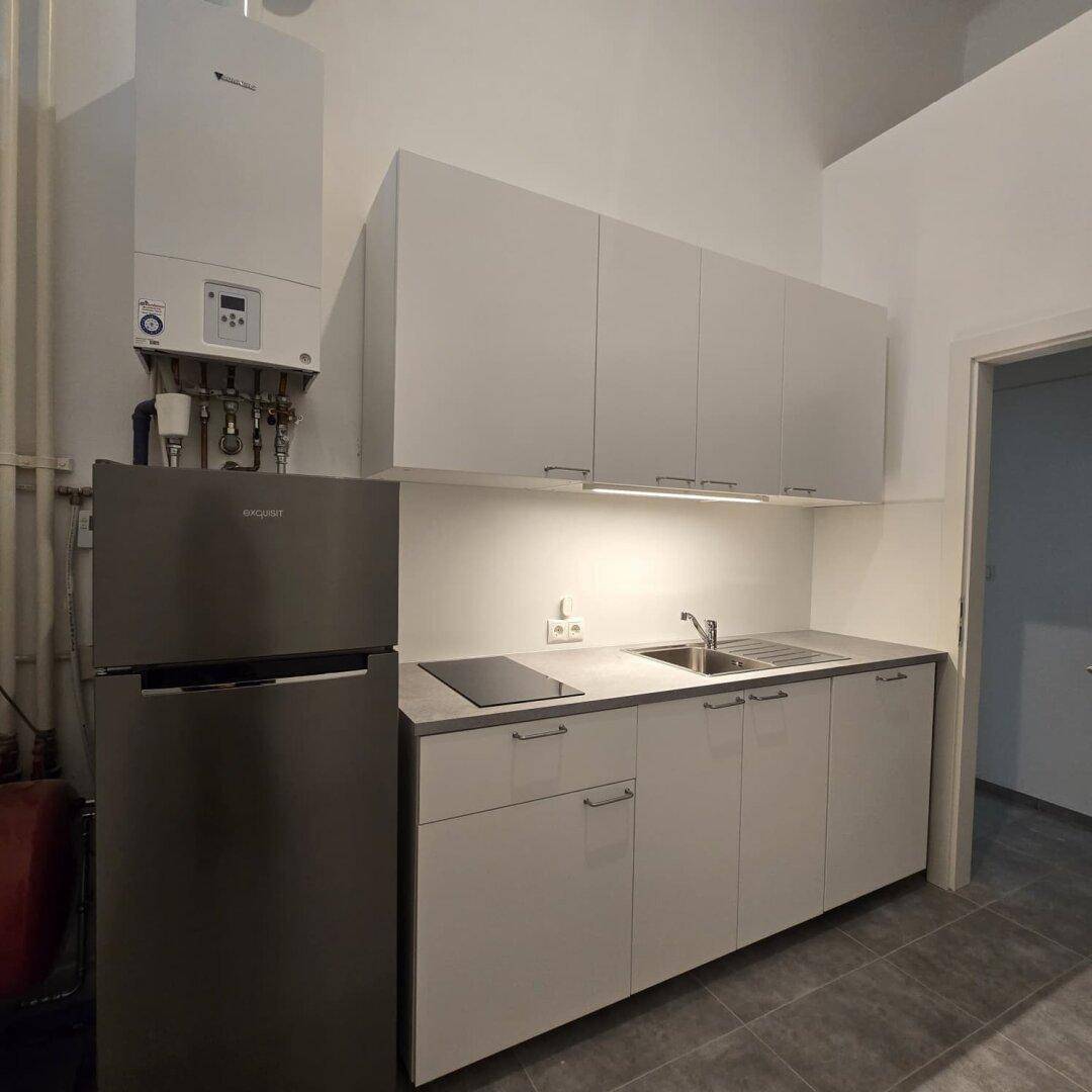 Neue Küchenzeile mit Kühlschrank, Spüle, Induktionskochfeld und Hängeschränken in minimalistischem Design.