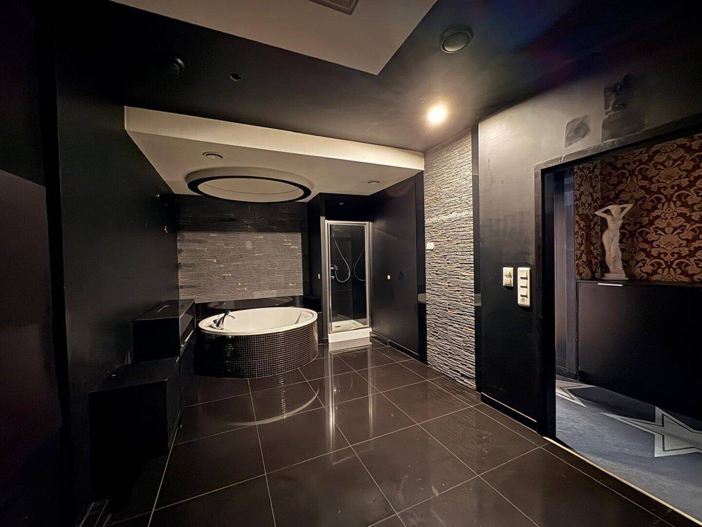 Großes Badezimmer mit dunklen Fliesen, runder Badewanne und Duschkabine, modern gestaltet.