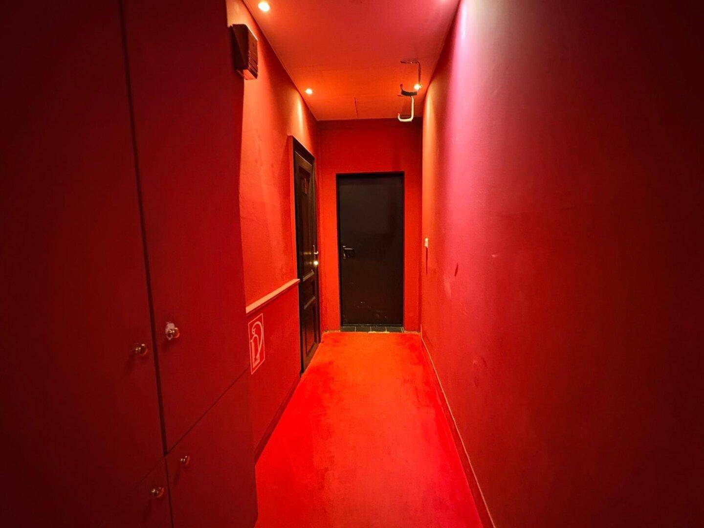 Roter Flur mit dunklen Türen und Schließfächern, beleuchtet von Deckenstrahlern.