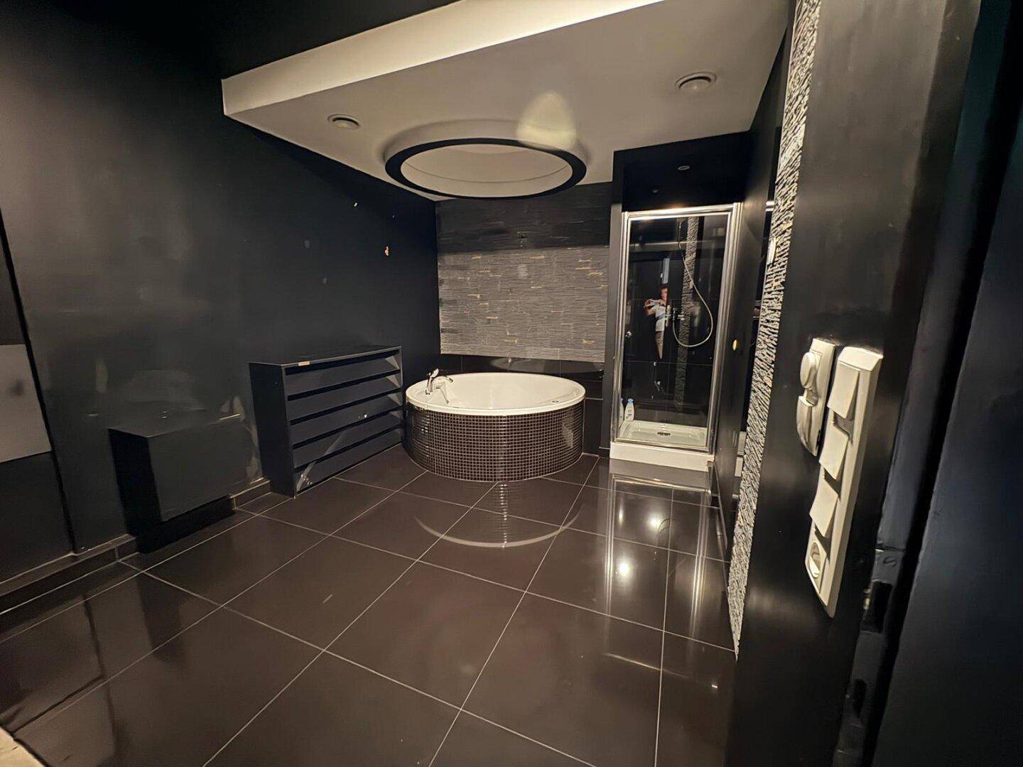 Geräumiges Badezimmer mit dunklen Fliesen, runder Badewanne und Duschkabine, mit schwarzem Schrank.