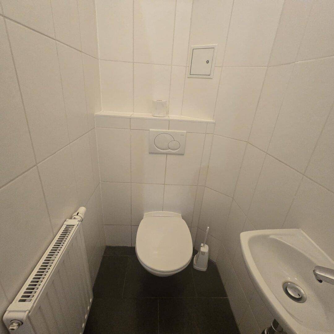 Kleines Gäste-WC mit weißen Fliesen, dunklem Boden und einer Toilette mit Waschbecken.