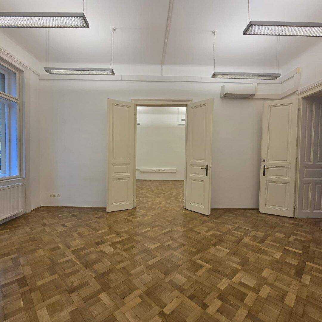 Großer Büroraum mit Parkettboden und mehreren Türen, die zu weiteren Räumen führen.