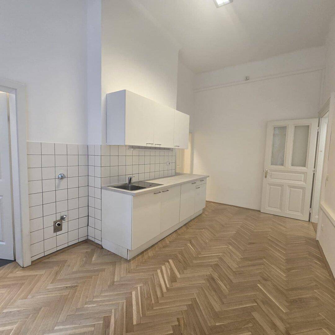 Einfache Küchenzeile mit weißen Schränken und Fliesen, bereit für die Installation von Geräten.