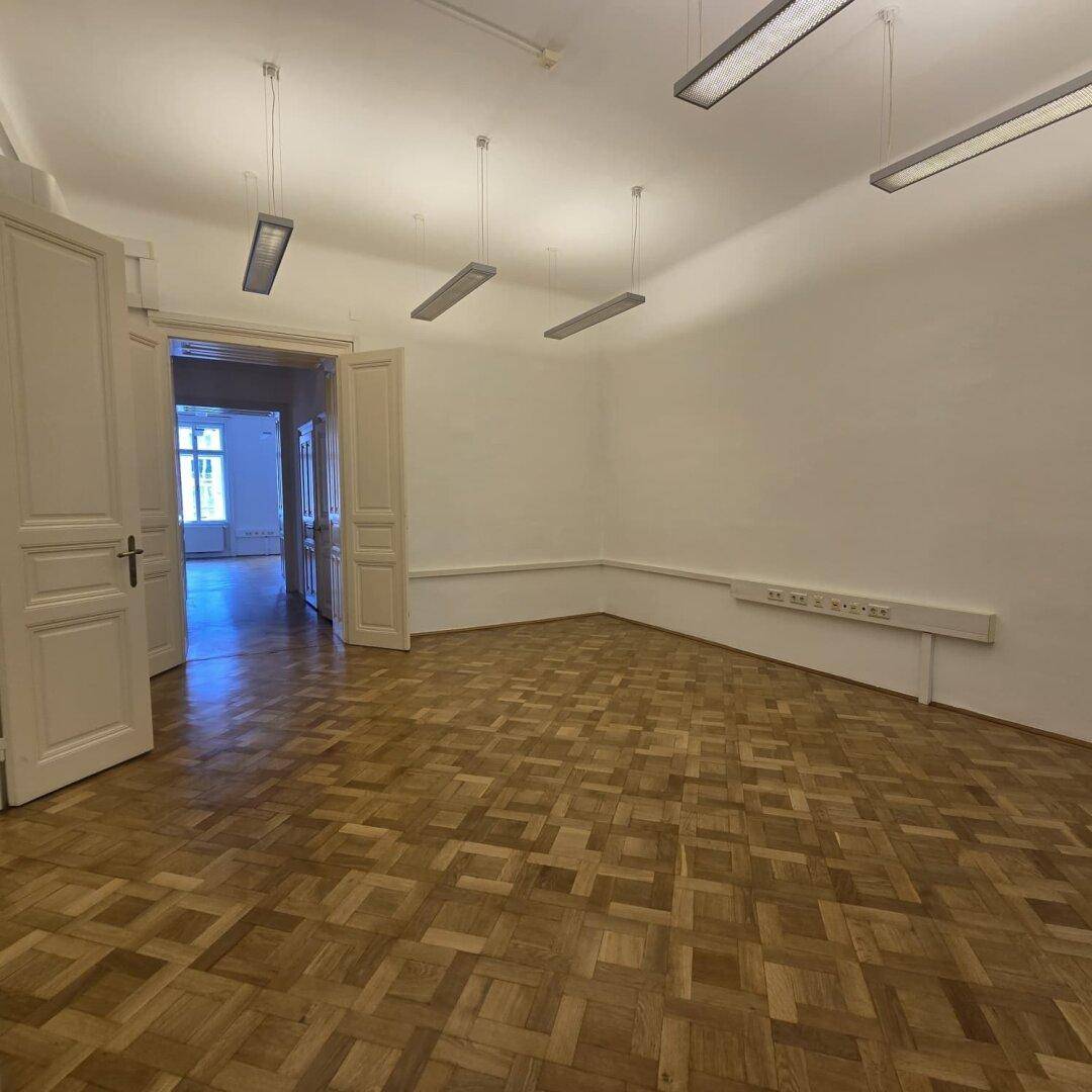 Heller Büroraum mit Parkettboden und hohen Decken, ideal für verschiedene Nutzungskonzepte.