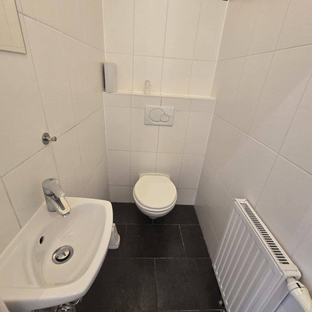 Separate Toilette mit Waschbecken und Heizkörper, in schlichtem Design gehalten.