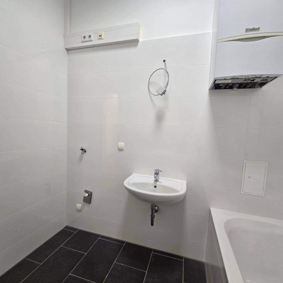 Helles Badezimmer mit Waschbecken und Badewanne, ausgestattet mit einer Gastherme.