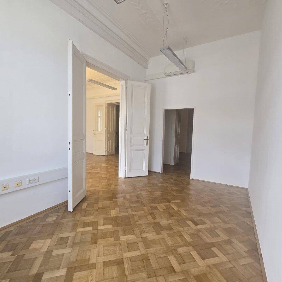 Geräumiger Büroraum mit Parkettboden und hohen Türen, der eine flexible Raumgestaltung ermöglicht.