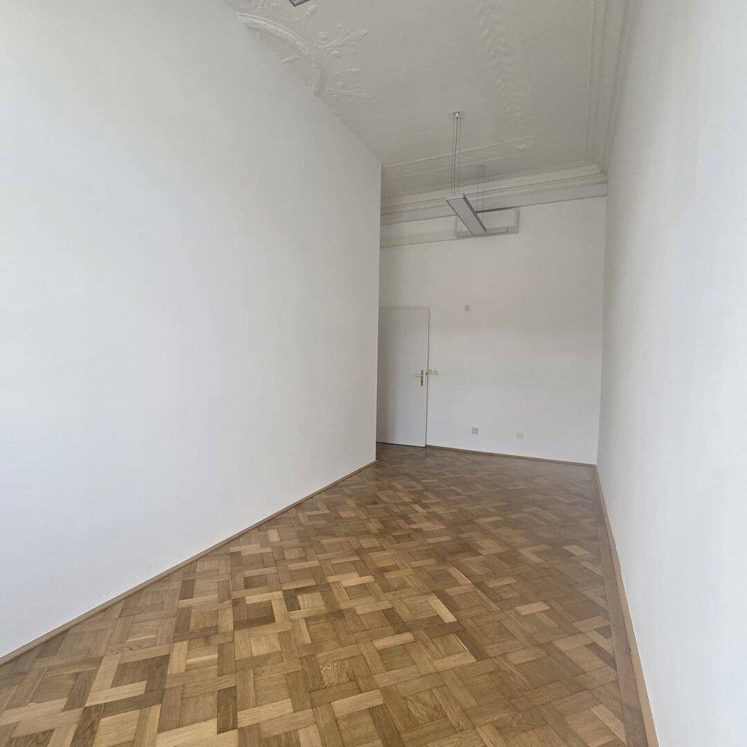 Leerer Büroraum mit Parkettboden und Stuckdecke, bereit für neue Mieter.