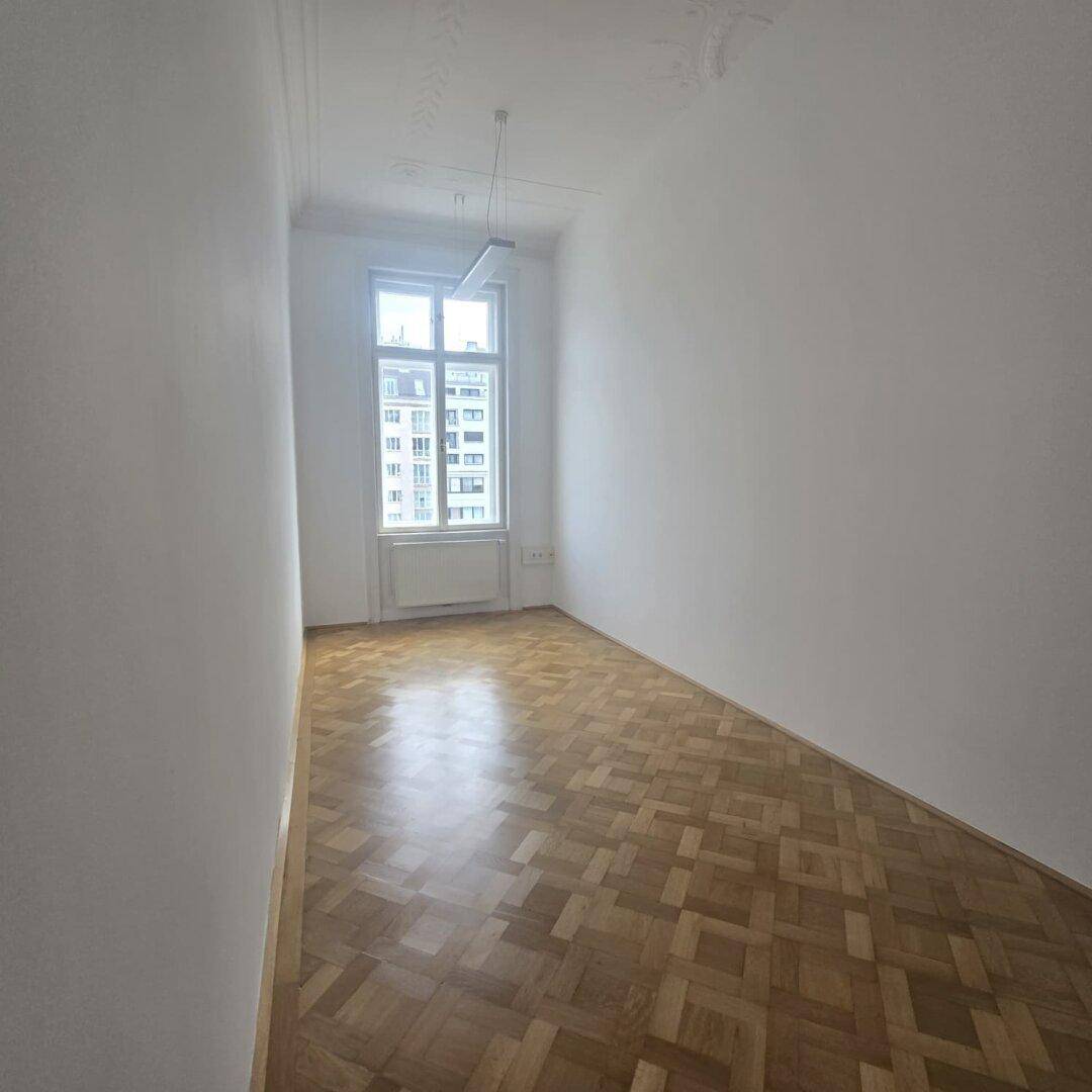 Heller Büroraum mit Parkettboden und einem großen Fenster, das viel Licht spendet.