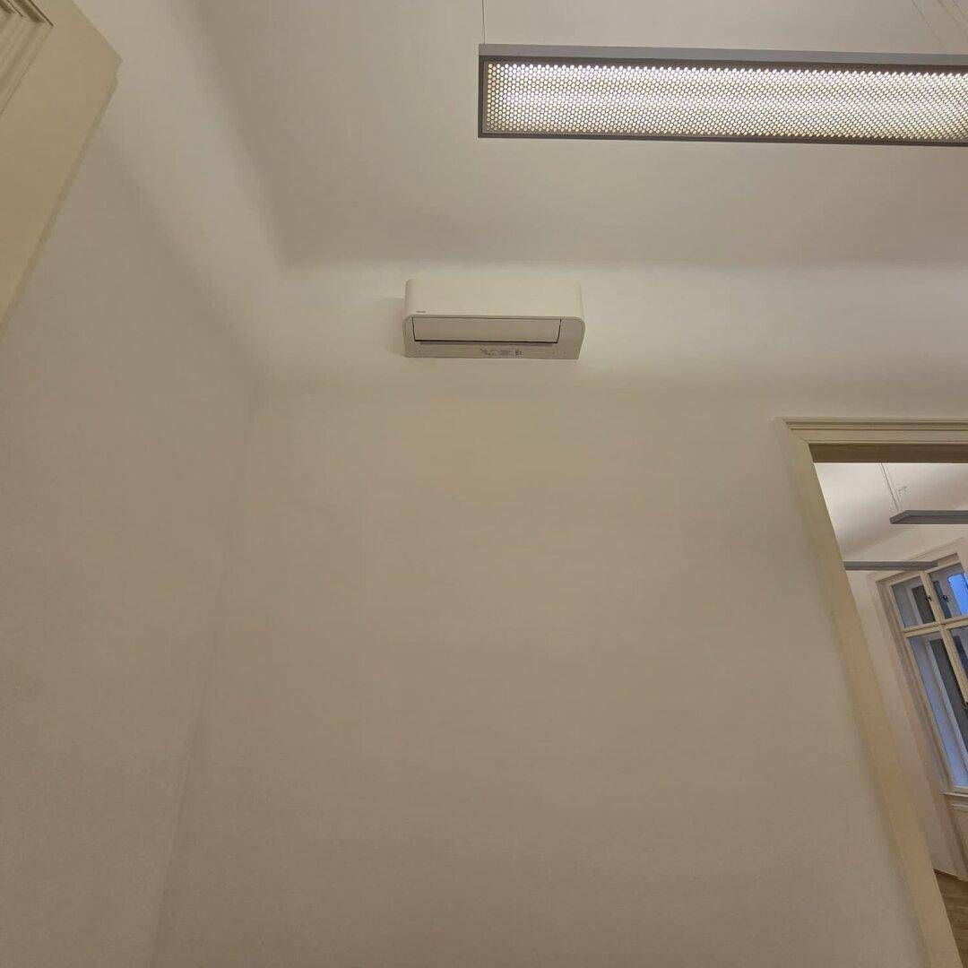 Detailaufnahme einer Klimaanlage an der Wand in einem hellen Büroraum.