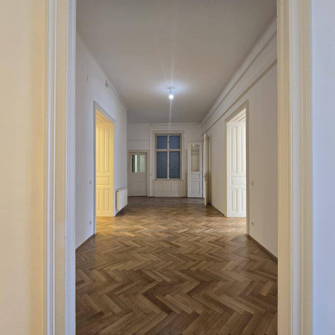 Großer Büroraum mit Fischgrätparkett und hohen Decken, der viel Tageslicht erhält.