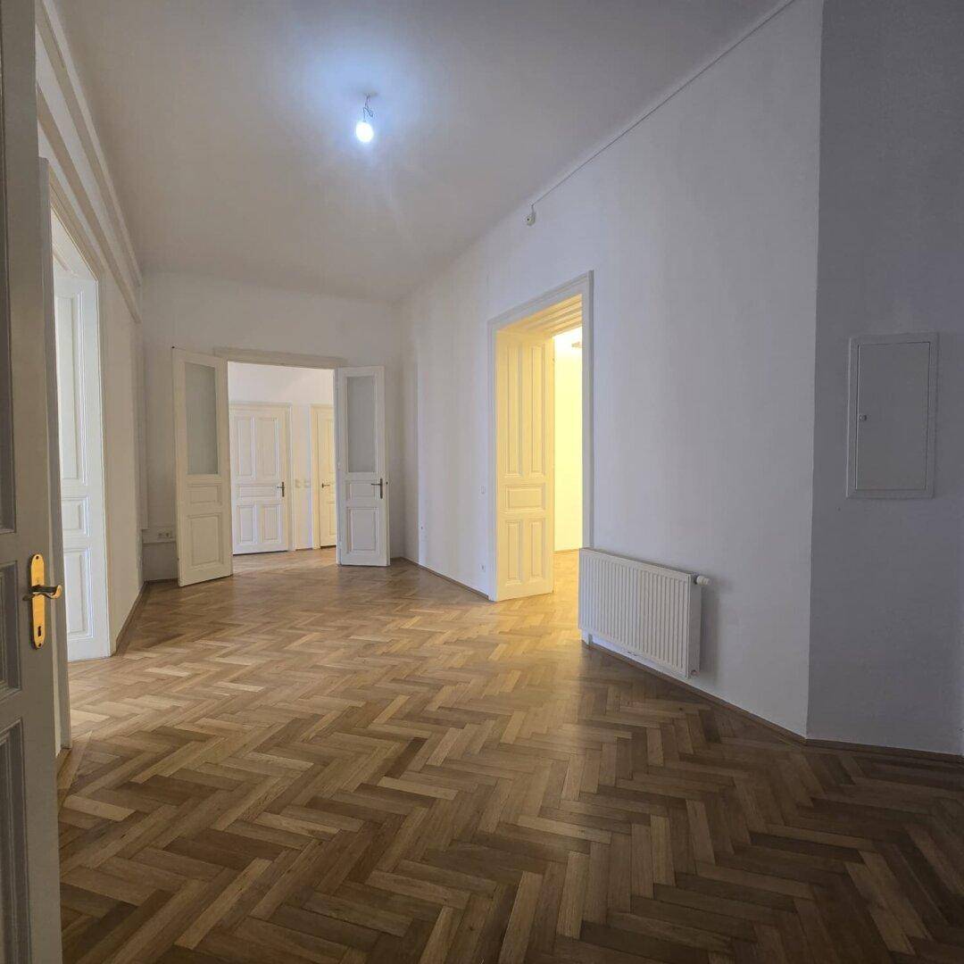 Geräumiger Büroraum mit Fischgrätparkett und hohen Decken, der viel Tageslicht erhält.