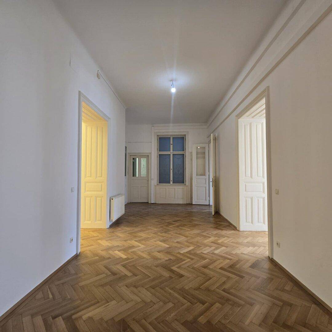 Langer Flur mit Fischgrätparkett und hohen Decken, der zu einem hellen Raum mit Fenster führt.