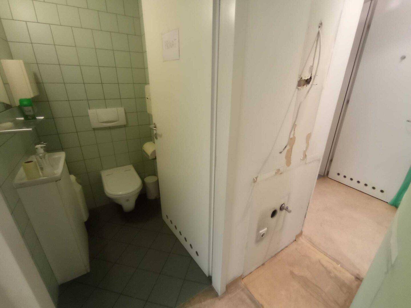 Kleines Gäste-WC mit hellgrünen Fliesen, Toilette und Waschbecken, funktional und sauber gehalten.