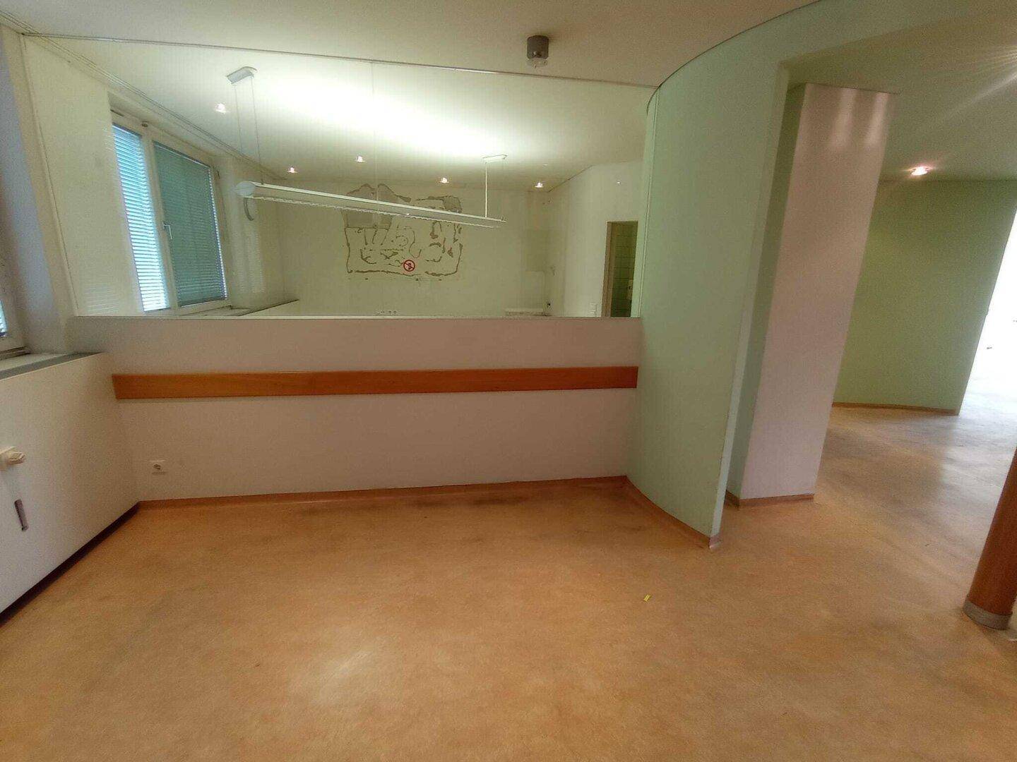Empfangsbereich mit geschwungener Wand, großem Spiegel und Fenstern mit Jalousien, bietet viel Potenzial.