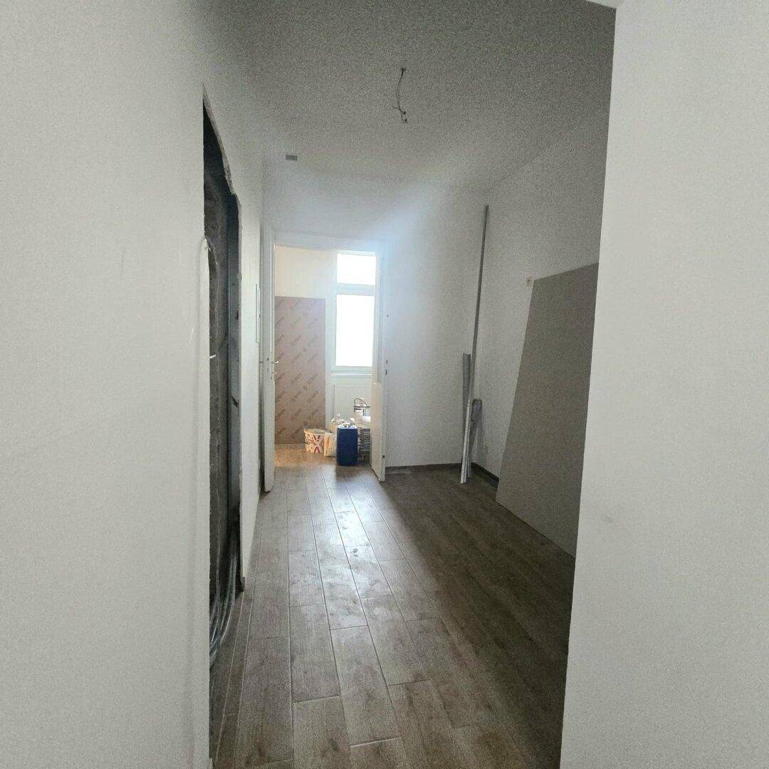 Flur im Renovierungszustand mit Holzboden, weißen Wänden und Baumaterialien, ein Fenster ist sichtbar.