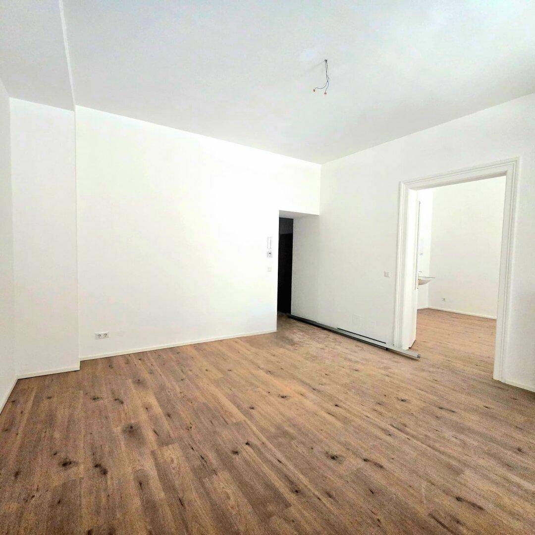 Leerer Raum mit Holzboden und weißen Wänden, mit Zugang zu einem angrenzenden Badezimmer.