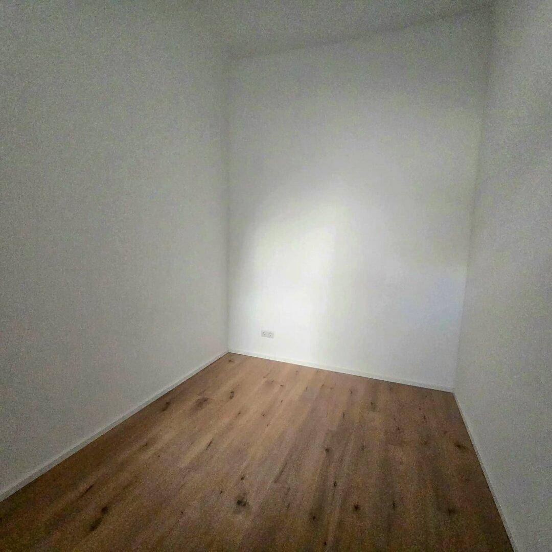 Kompakter, leerer Raum mit Holzboden und weißen Wänden, der vielseitig genutzt werden kann.