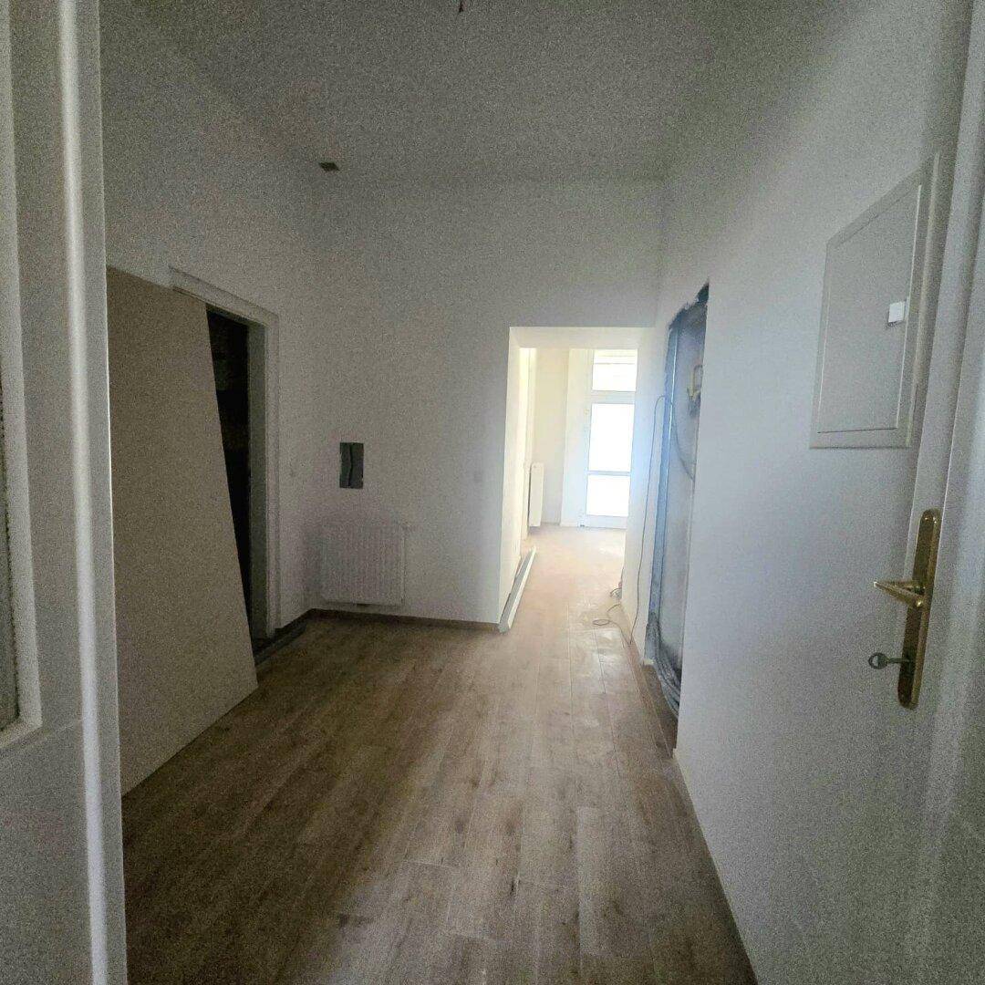 Flur im Renovierungszustand mit Holzboden und weißen Wänden, mit offener Tür und sichtbaren Baumaterialien.
