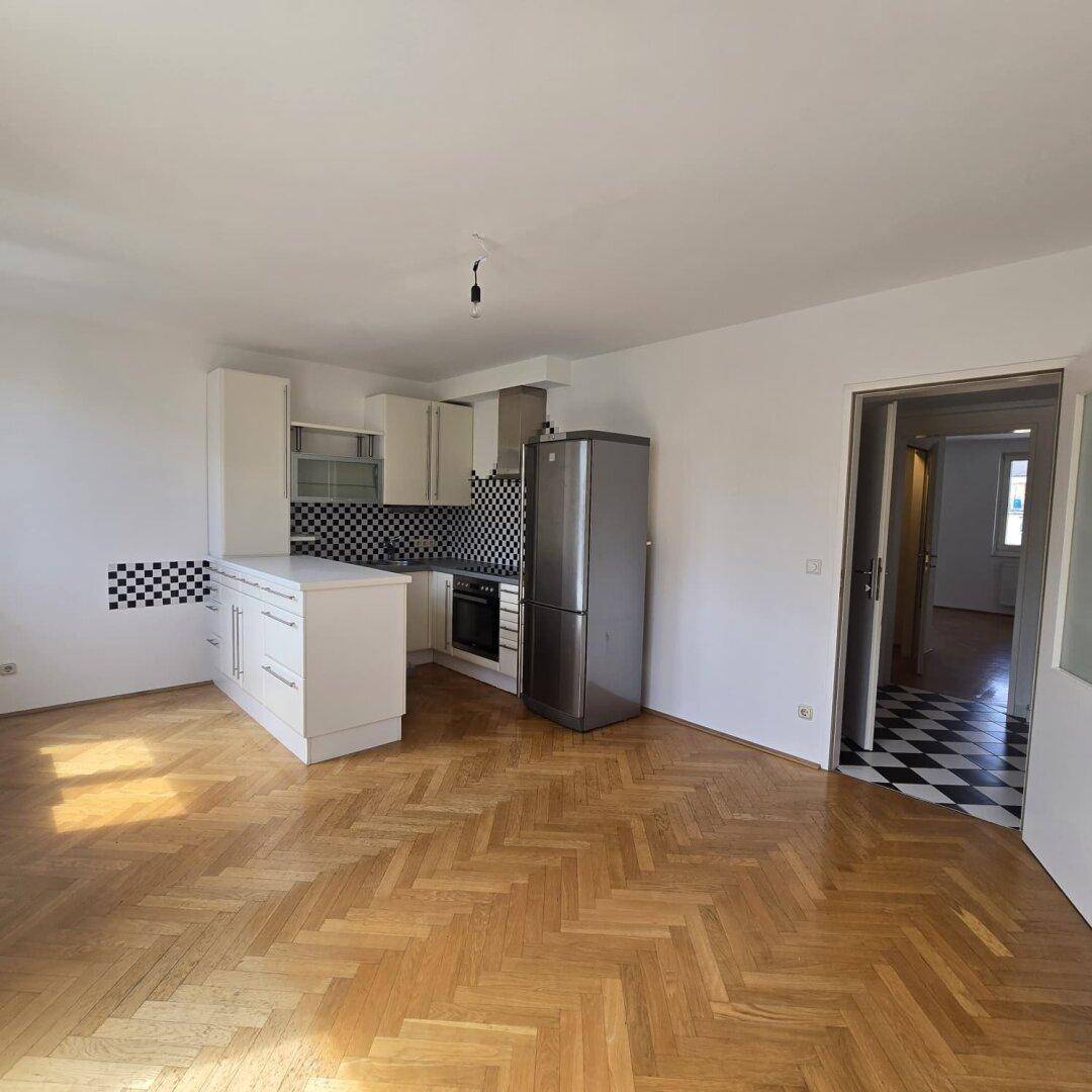 Offener Wohnbereich mit Fischgrätparkett und integrierter Küche mit schwarz-weißem Fliesenspiegel.