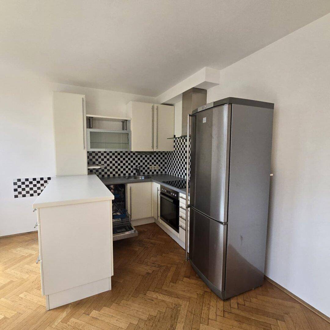 Funktionale Küche mit weißen Einbauschränken, Edelstahlkühlschrank und schwarz-weißem Fliesenspiegel.