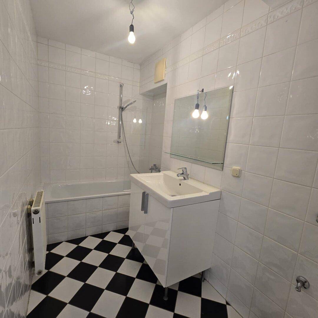 Badezimmer mit weißen Fliesenwänden, schwarz-weißem Schachbrettmuster-Fliesenboden, Badewanne und Waschtisch.