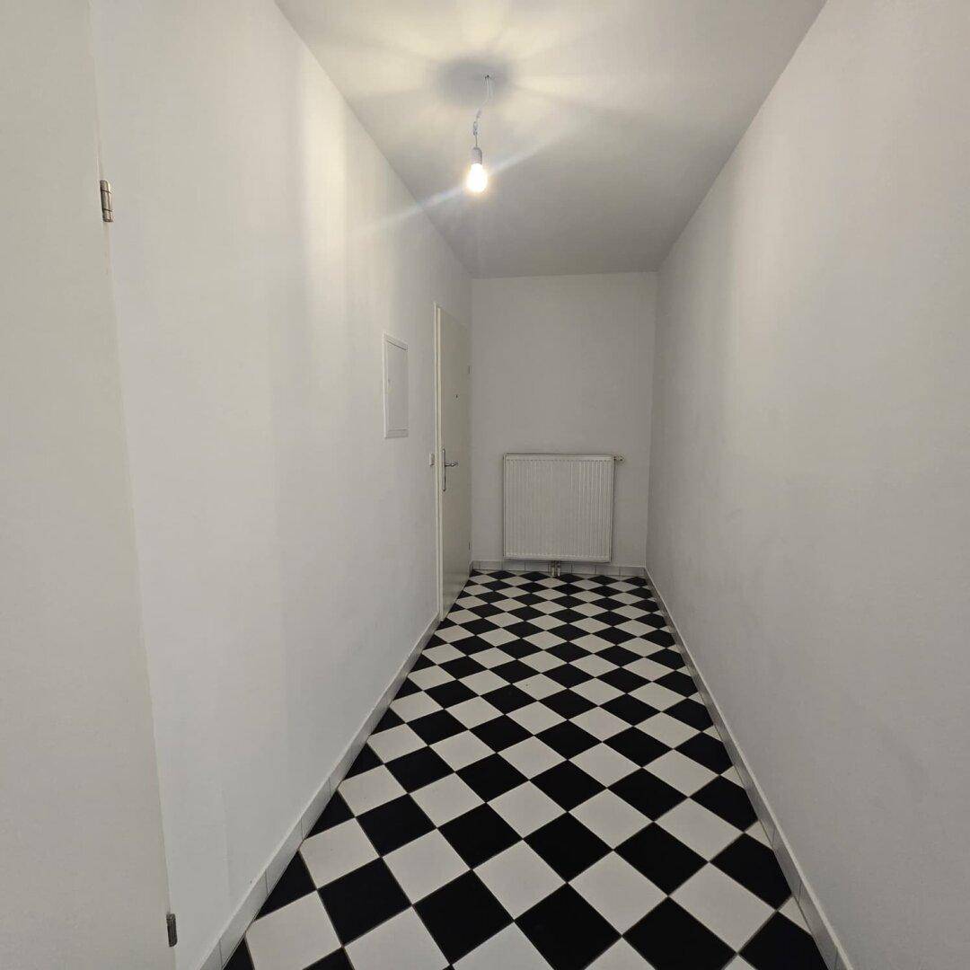 Langer Flur mit markantem schwarz-weißem Schachbrettmuster-Fliesenboden und weißen Wänden.